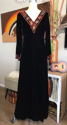 Absolutely gorgeous!  Late 1960's Black Velvet A-Line Maxi Dress by Toni Todd Beautifully made, elegant style 10" Deep V Neckline Trimmed in 2" Wide Multi Color Floral Embroidery Fully Lined in Black Nylon Fabric 15 " Back Zipper MEASUREMENTS (in inches):                                                                                                                    Shoulder to Shoulder from the back 15" Bust : 38" Waist: 34" Hips: 48" Side Length underarm to hem 51" Arm Length underarm to cuff 16" 2" Embroidery Design Cuff Neck Opening:  Front V Back of Neck to Hem 51" front - 50" Skirt Circumference 92" INTERNATIONAL CUSTOMER?? Please email for Shipping Info Traditional Fall Party Dresses, Vintage Embroidered Costume Dress, Traditional Formal Dress For Fall, Retro Long Sleeve Vintage Dress For Costume, Retro Long Sleeve Vintage Costume Dress, Vintage Embroidered Fall Dresses, Vintage Fall Costume Dresses, Vintage Dress For Fall Costume, Vintage Costume Dress For Fall