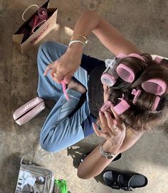 a woman sitting on the ground with pink hair rollers in her hands and other items around her