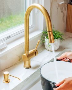 a person washing their hands under a faucet in a kitchen sink next to a window