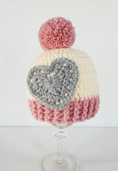 a crocheted hat with a heart on the front and two pom - poms on the back