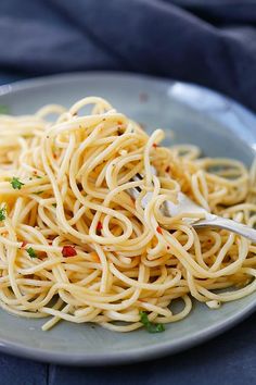 a white plate topped with spaghetti on top of a blue table cloth next to a fork