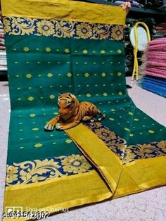 a tiger laying on top of a green and yellow blanket next to stacks of shirts