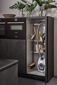 an open cabinet with some plants in it and a vacuum on the floor next to it