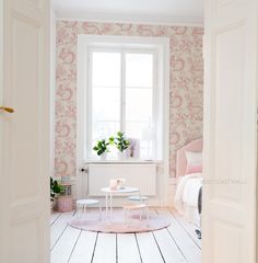 an open door leading to a bedroom with pink wallpaper and white flooring on the walls