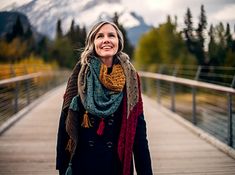 a woman standing on a bridge with mountains in the background and trees around her, smiling