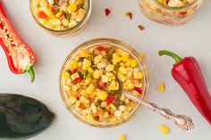 two glass jars filled with corn next to peppers and jalapenos on a white surface