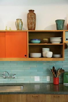 a kitchen with orange cabinets and dishes on the shelf above the sink is filled with utensils