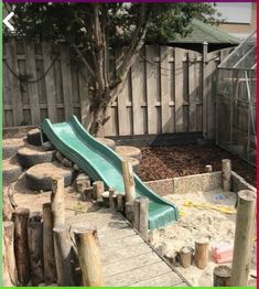 there is a green slide in the sandbox next to a wooden fence and tree