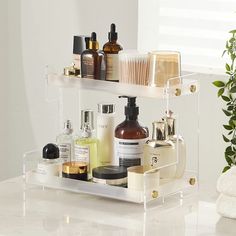 two clear shelves holding various beauty products on a white countertop next to a potted plant