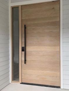 a modern wooden door on the side of a white house with glass panels and black handles