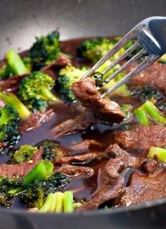 beef and broccoli being cooked in a skillet with a spatula on top