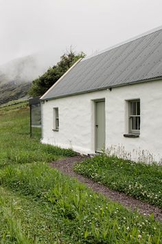 a small white house sitting on top of a lush green hillside next to a field