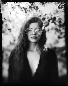 black and white photograph of a woman with long hair wearing glasses in front of trees