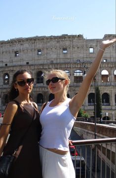 two women standing next to each other in front of an old building with a roman collise