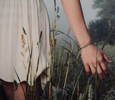 a woman in a white dress is walking through tall grass with her hand on the ground