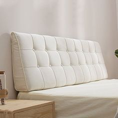 a bed with a white headboard sitting next to a plant on a wooden table