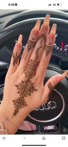 a woman's hand with henna tattoos on her left wrist and the inside of her car steering wheel