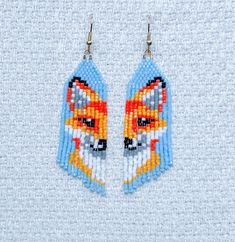 the beaded earrings are decorated with an orange and blue fox head on it's side