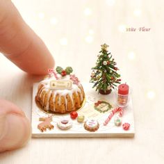 a miniature christmas cake with icing and candy on it's plate next to a small tree