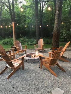 a fire pit surrounded by wooden chairs in the middle of a gravel area with string lights hanging above it