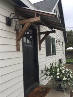 a white house with a black door and some flowers on the front porch, next to it is a potted plant