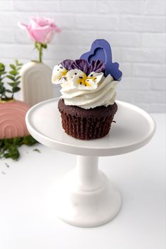 there is a cupcake with white frosting and purple flowers on the cake stand