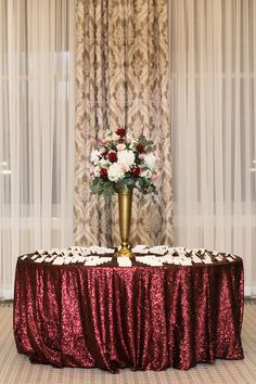 a vase with flowers on top of a table in front of sheer drapes and curtains