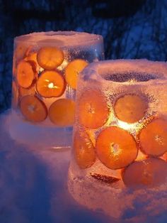 two lit candles sitting in the snow with oranges on them and ice around them