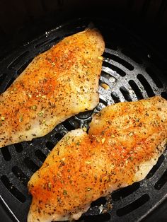 two pieces of chicken are cooking in an air fryer with seasoning on top