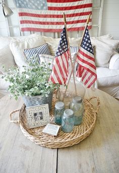 two american flags are on the table in front of a basket with jars and candles