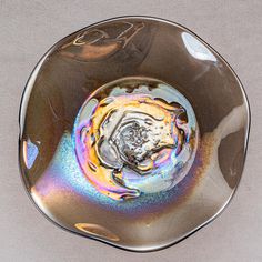 a silver plate with multicolored swirls in the center on a gray surface