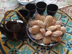 a plate topped with cookies next to cups and a tea pot on top of a table