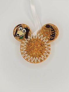 a mickey mouse ornament hanging from a white ribbon with gold glitter on it