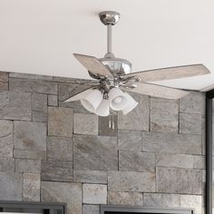 a ceiling fan that is mounted to the side of a stone wall with three lights