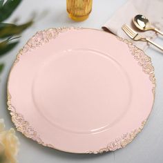 a pink plate with gold trim sits on a table next to silverware and flowers