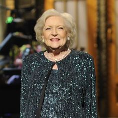 an older woman wearing a black and green dress standing in front of a piano on stage