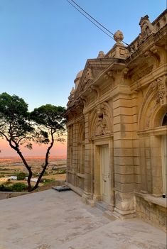 an old building with a tree in front of it and the sun setting behind it