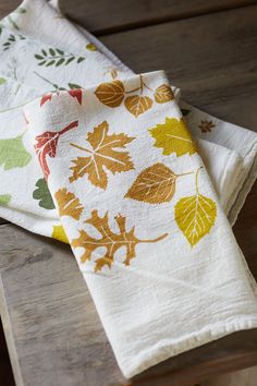 two napkins with leaves on them sitting on a wooden table