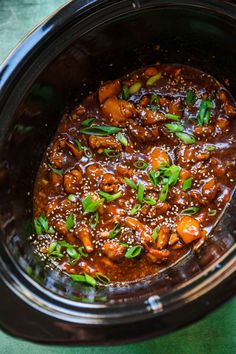 a crock pot filled with meat and veggies on top of a green table