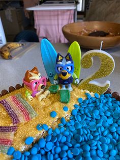 there is a cake that looks like it has two figures on top and blue pebbles in the bottom