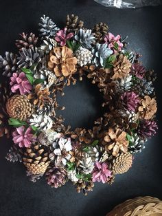 a wreath made out of pine cones and artificial flowers on a table next to a basket