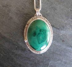 "Here is a handmade pendant made with a lovely malachite and sterling silver. The stone is oval in shape and bright green with a subtle pattern within and a perfect polish.  I set the stone in a fine silver bezel with a sterling silver back plate that I textured around the edge.  I added a little ball of recycled silver at the side.  The pendant measures approx. 1\" by 1 1/2\" (37mm by 27mm) The sterling silver chain is 20\" long with a lobster clasp." Green Sterling Silver Oval Cabochon Jewelry, Green Oval Malachite Necklaces, Green Oval Malachite Necklace, Green Oval Malachite Jewelry, Oval Green Malachite Jewelry, Green Oval Necklace With Large Stone, Oval Green Necklace With Large Stone, Green Oval Large Pendant Jewelry, Lavender Silk