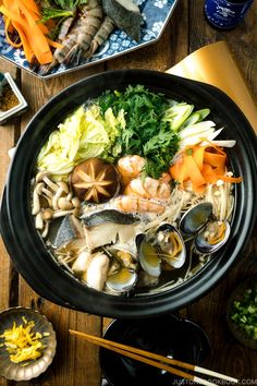 a bowl filled with seafood and vegetables next to chopsticks on top of a wooden table