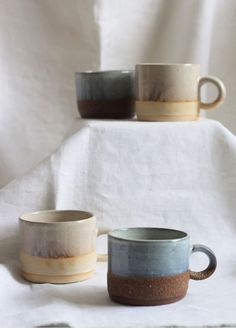 three coffee cups sitting on top of a white cloth covered table next to each other