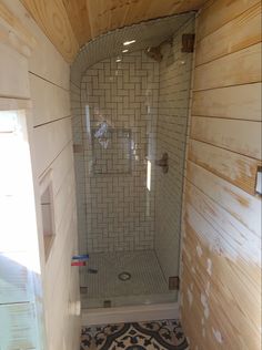 a shower in a small bathroom with wood paneling on the walls and floor, next to a window