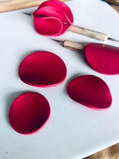 three red pieces of paper sitting on top of a white surface next to some knitting needles