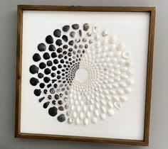 a white framed artwork with black and white pebbles in it on the wall next to a potted plant