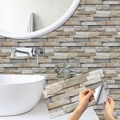 a person is holding a mirror in front of a bathroom wall with stone tiles on it