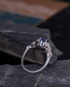 a silver ring with blue sapphire stones on top of a stone slab in front of a book