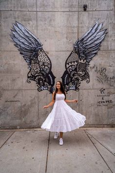 a woman standing in front of a wall with two wings painted on it's side